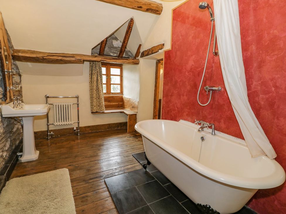 A bathroom with a clawfoot bathtub shower white sink wooden floor and a window seat at Ysgubor in Dinas Mawddwy near Dolgellau