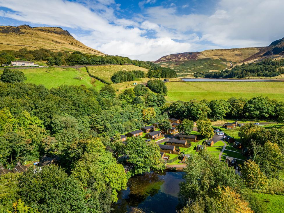 An aerial view of cabins and trees near a body of water surrounded by hills at Dovestone Pod 18 in Greenfield