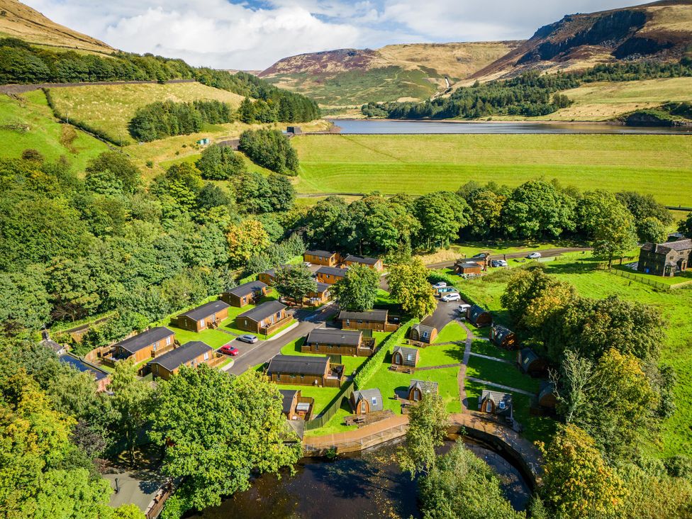 An aerial view of a holiday park with wooden cabins and pods surrounded by trees hills and a reservoir at Dovestone Pod 21 in Greenfield