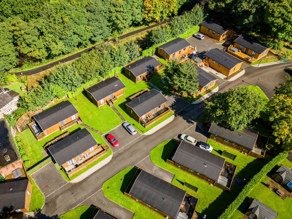 An aerial view of a residential area with wooden cabins green lawns trees and parked cars at Dovestone Pod 21 in Greenfield