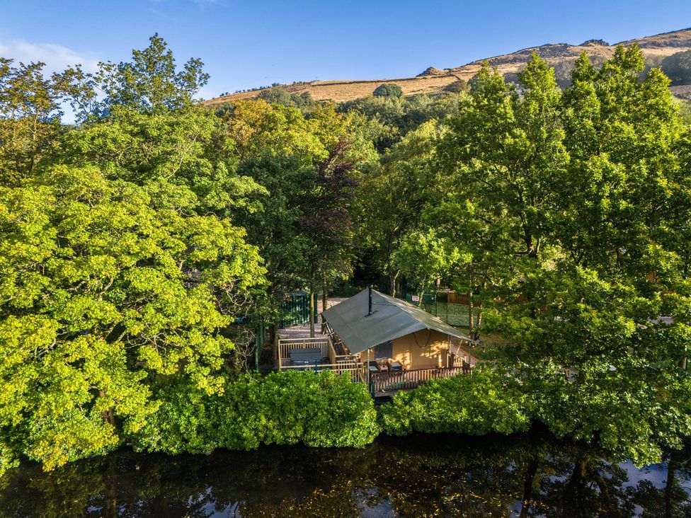 A tent cabin surrounded by trees near a body of water at Dovestone Pod 21 in Greenfield
