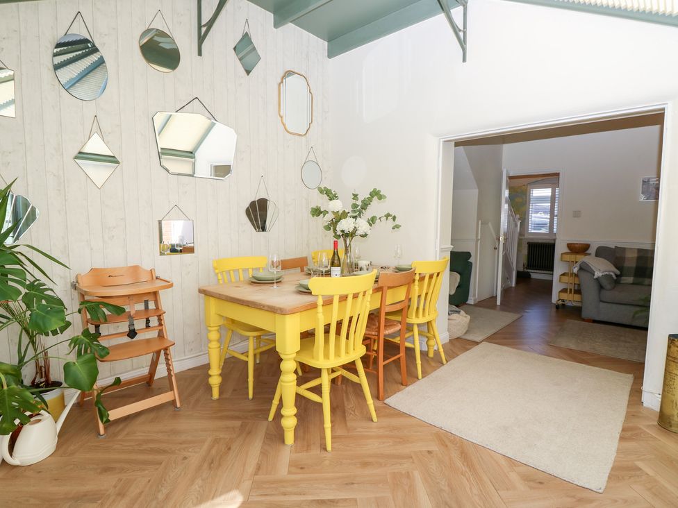 A dining area with a yellow table and chairs a wooden high chair and multiple mirrors on the wall at 3 West Quay Mews in Poole