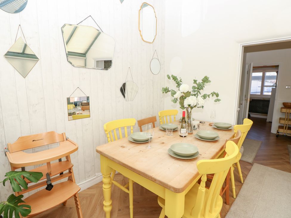 A dining room with a wooden table and yellow chairs with plates glasses and flowers on the table at 3 West Quay Mews in Poole