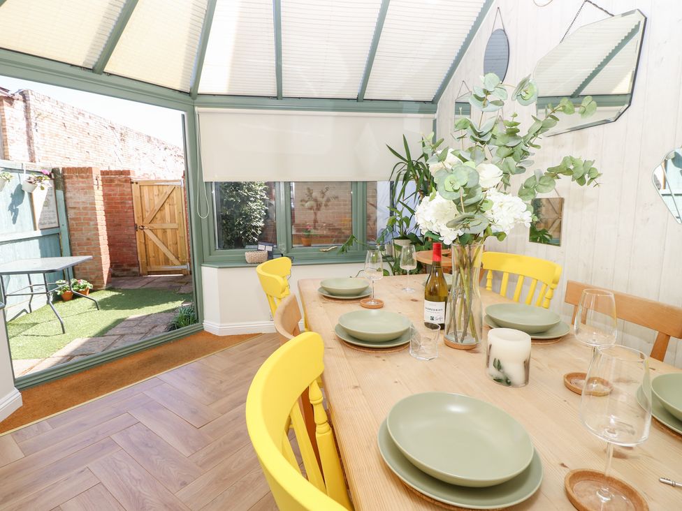 A dining area with a wooden table set for four with green plates yellow chairs and a vase of flowers at 3 West Quay Mews in Poole