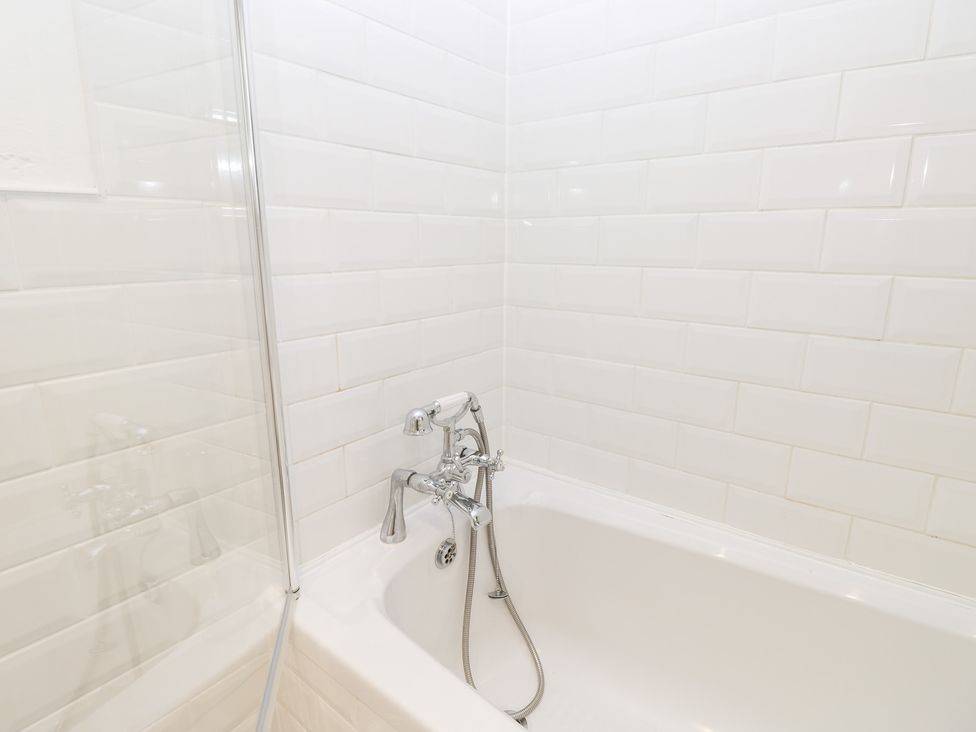 A bathtub with a handheld shower and white tiled walls at 3 West Quay Mews in Poole