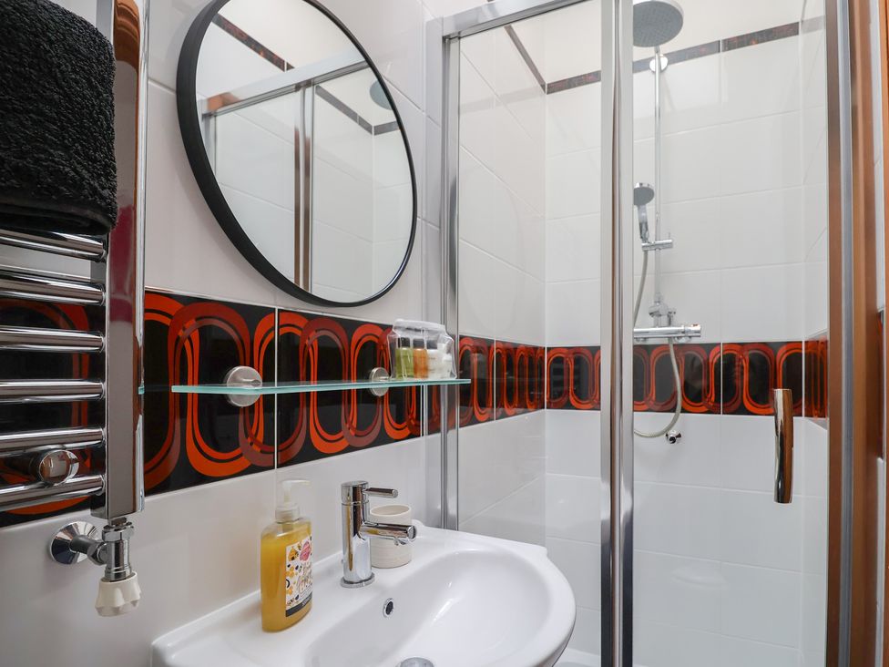 A bathroom with a sink a round mirror towel rack and a shower with glass door at Poppy Cottage in Aylesbeare