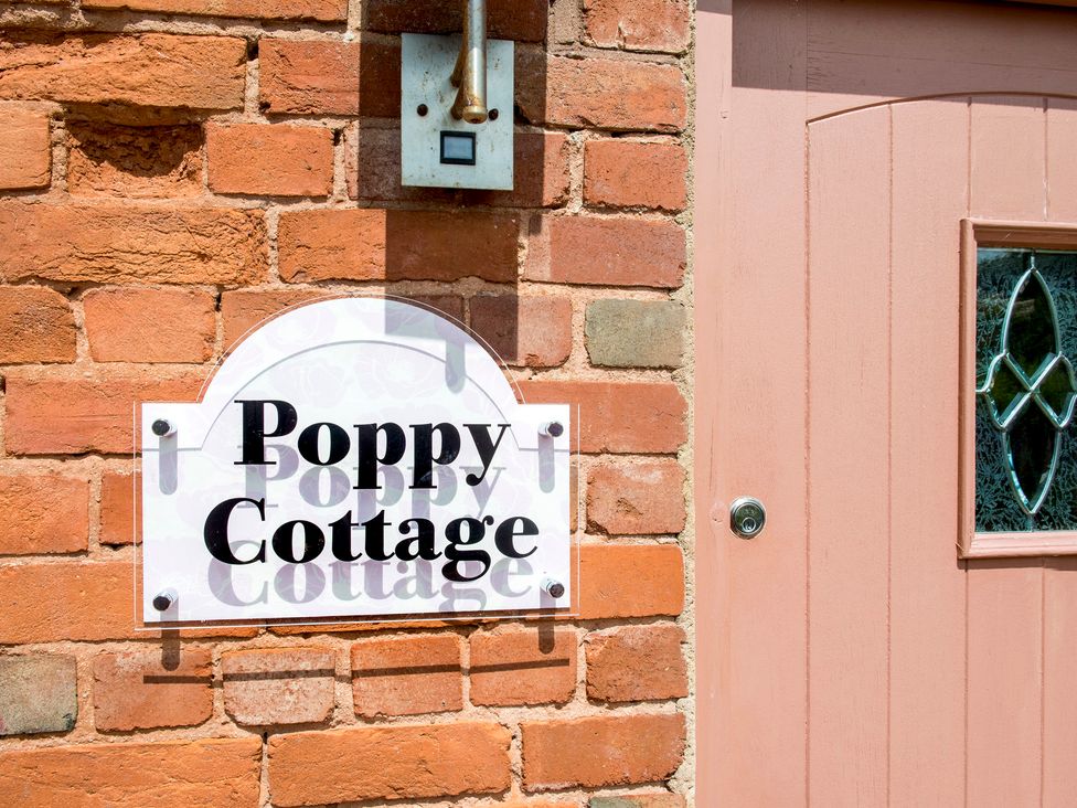 A brick wall with a white sign reading Poppy Cottage next to a pink door with a decorative glass panel at Poppy Cottage in Aylesbeare