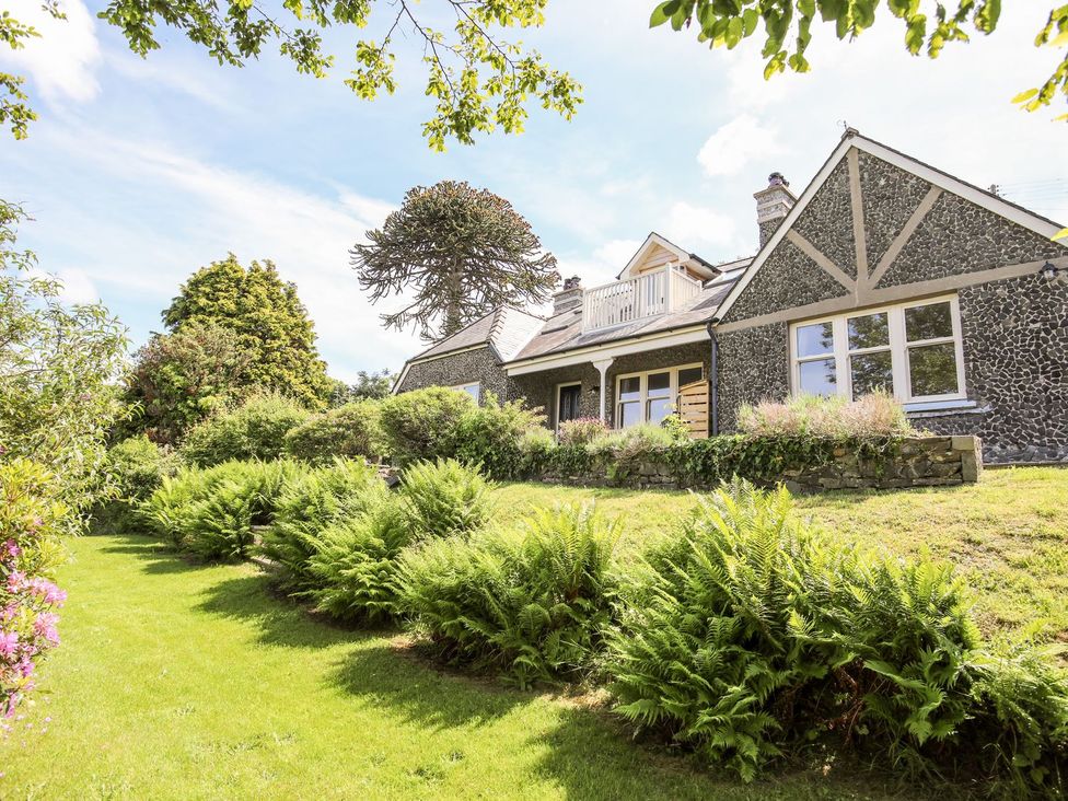 A stone house with a grass lawn and bushes in the garden at Bryn Awelon in Harlech