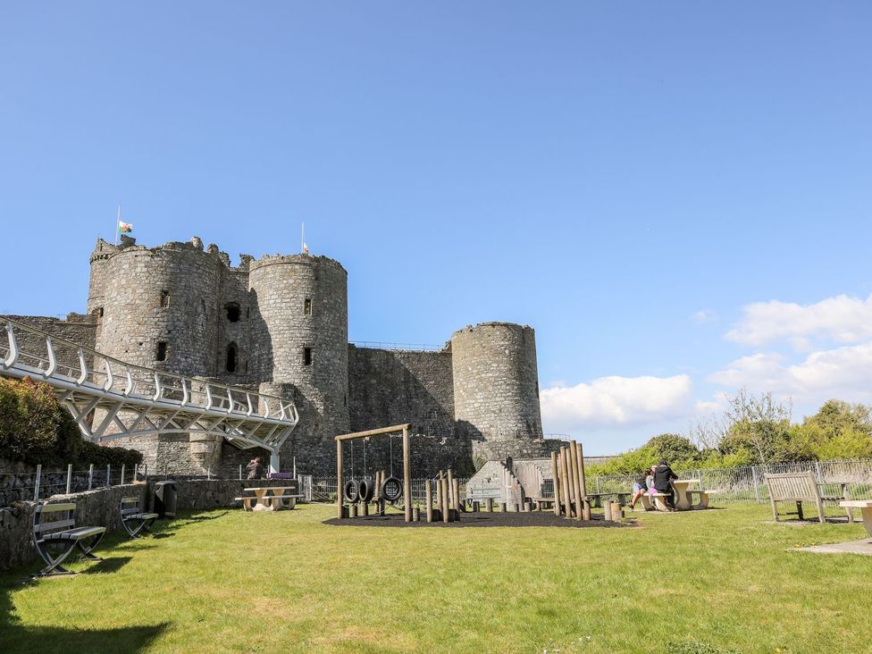 A playground with swings and benches near a stone castle at Bryn Awelon in Harlech
