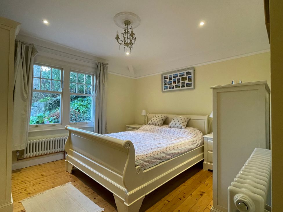 A bedroom with a cream bed and bedside tables near a window with curtains at Bryn Awelon in Harlech