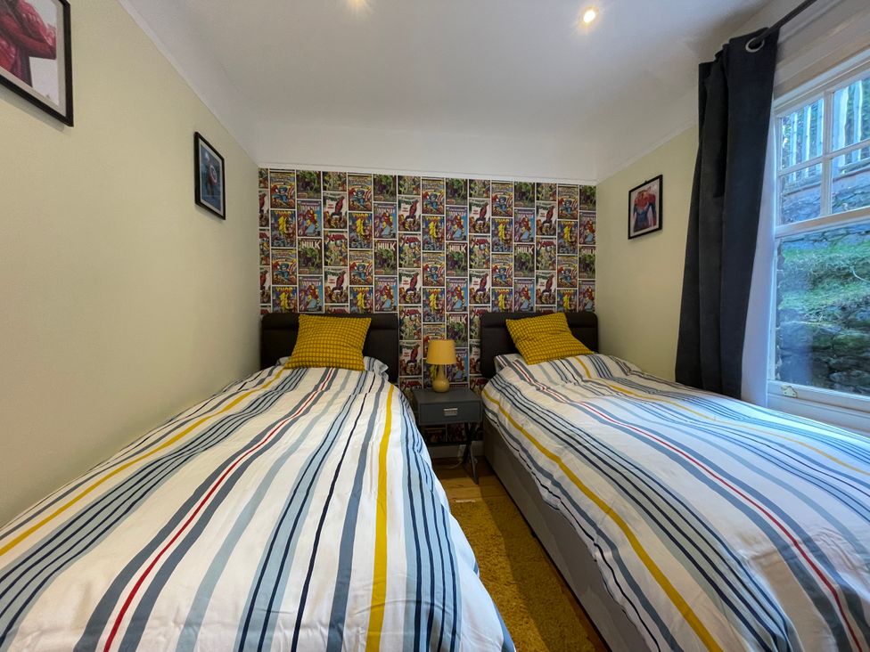 A bedroom with two single beds with striped bedding and superhero wallpaper behind at Bryn Awelon in Harlech