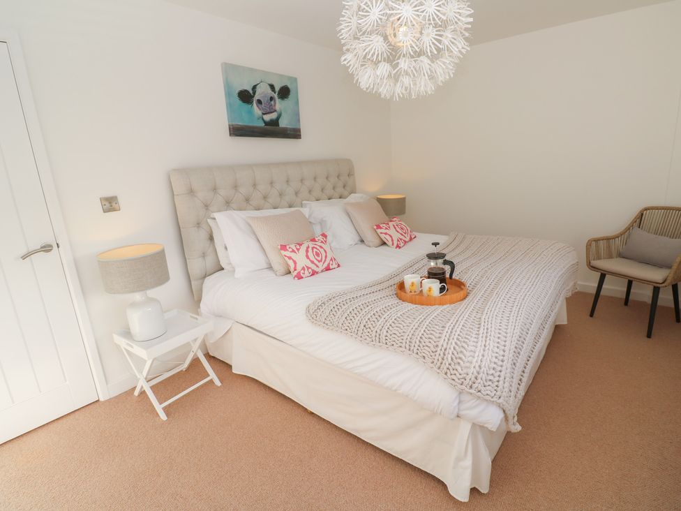 A bedroom with a bed with pillows and a blanket a chair bedside tables with lamps and a painting of a cow at The Duck House in Gulval near Penzance