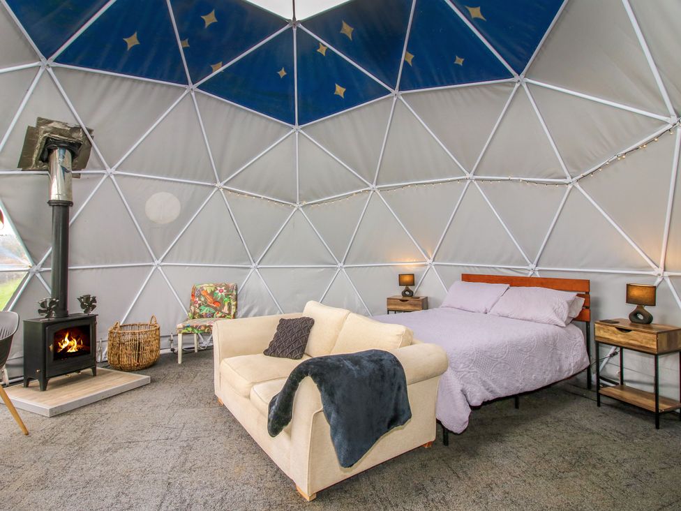 A dome-shaped room with a bed, sofa, wood burning stove, and a small chair at Meadow View - Bryn-Mawr Retreat in Brynmawr near Llanymynech