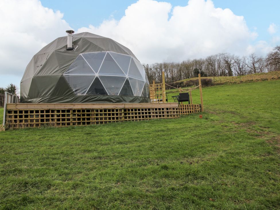 A geodesic dome on a wooden raised platform in a grassy field with trees in the background at Meadow View - Bryn-Mawr Retreat in Brynmawr near Llanymynech