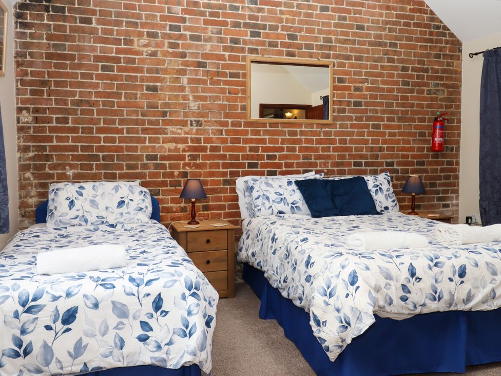 A bedroom with two beds with blue and white leaf patterned bedding a wooden nightstand and lamps against a brick wall at Daisy Cottage in Whitchurch Canonicorum near Charmouth