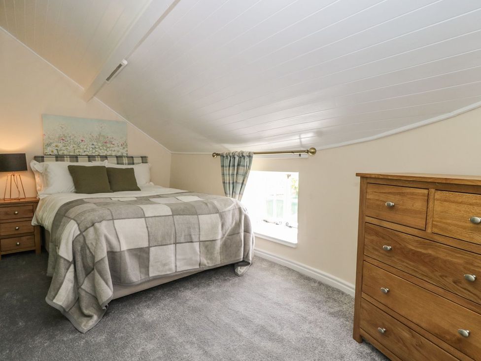 A bedroom with a bed and wooden dresser under a slanted ceiling at St Edmunds House in Crakehall