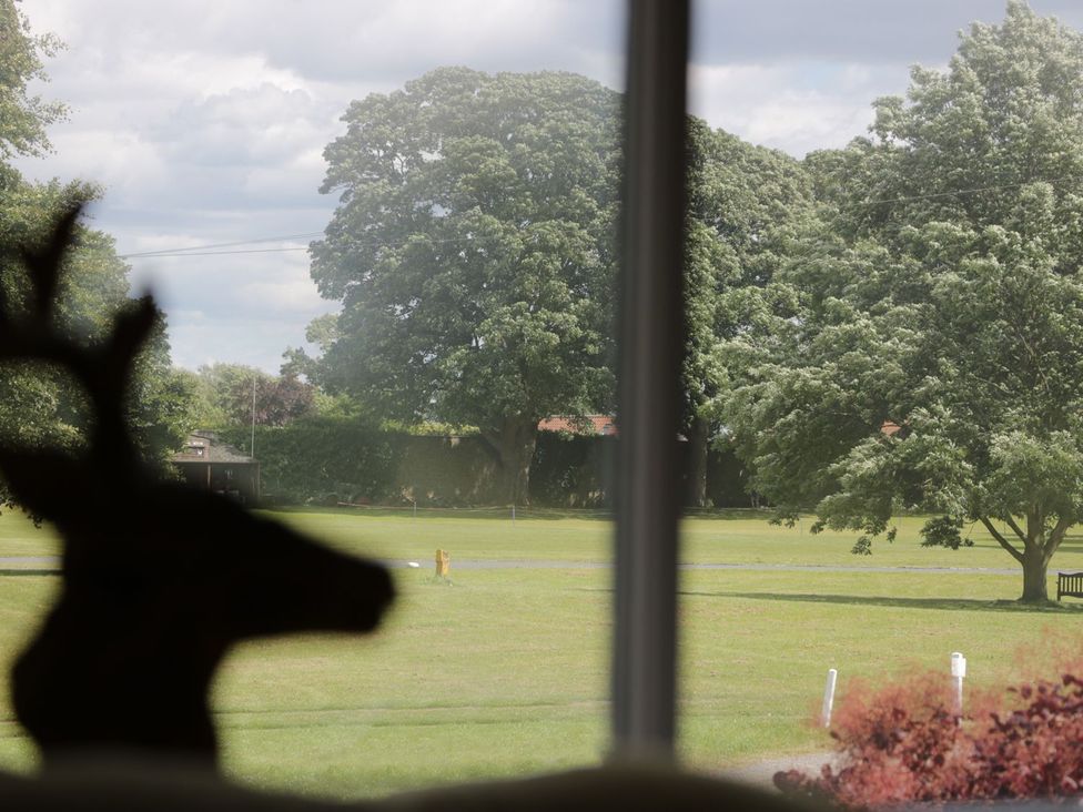 A view of a grassy field with large trees seen through a window with a silhouette of a deer figurine at St Edmunds House in Crakehall