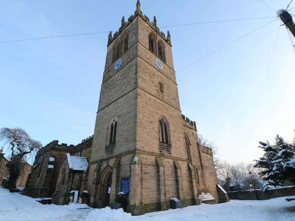 A stone church with a tall clock tower in a snowy outdoor setting at St Edmunds House in Crakehall