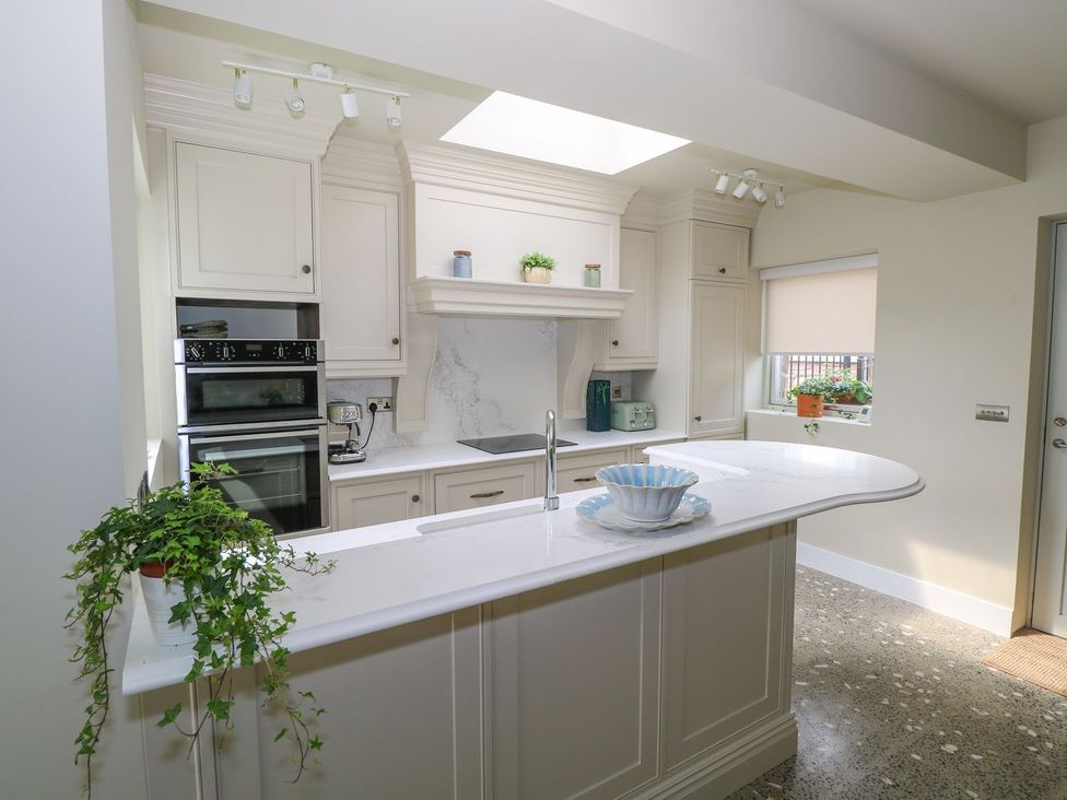 A modern kitchen with white cabinets a marble countertop a built in oven a sink and plants at Neds Cottage in Mulranny County Mayo