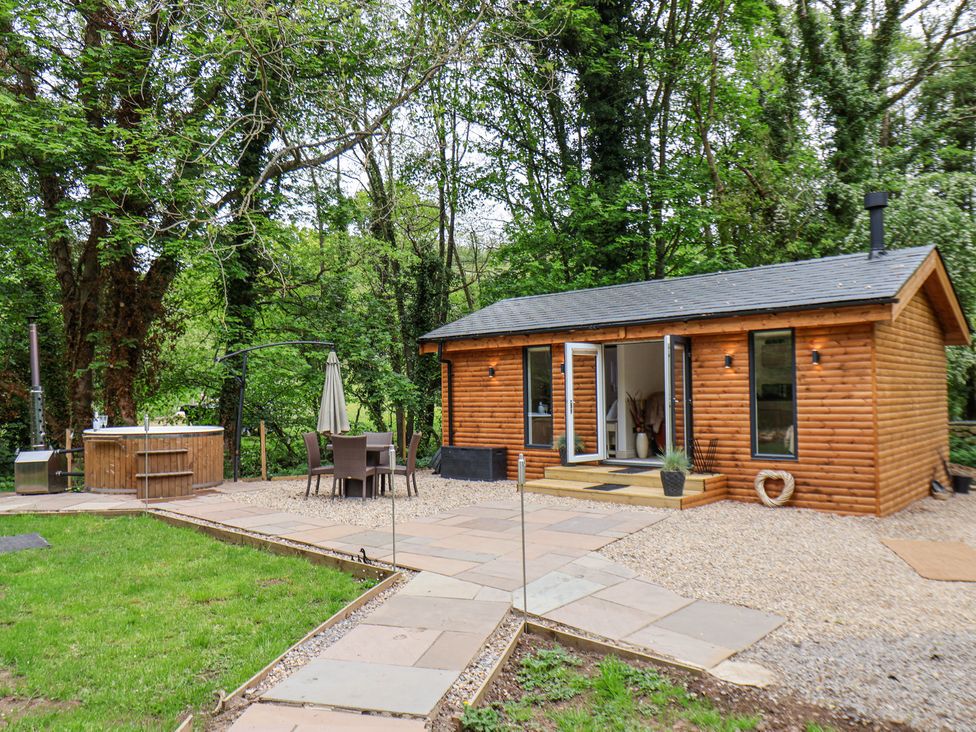 A wooden cabin with open doors a patio with a table and chairs and a hot tub in a garden at Roe Deer Lodge Littlebeck near Sleights