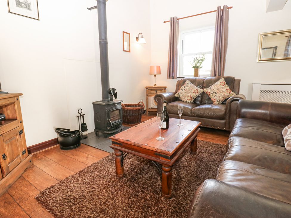 A living room with leather sofas a wood stove and a wooden coffee table at Pencroft Cottage in Carperby