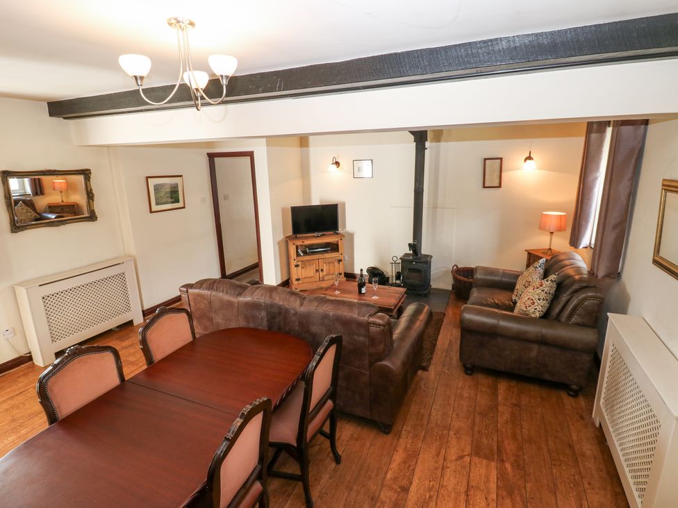 A living room with brown leather sofas a wooden dining table and chairs a wood stove and a television at Pencroft Cottage in Carperby