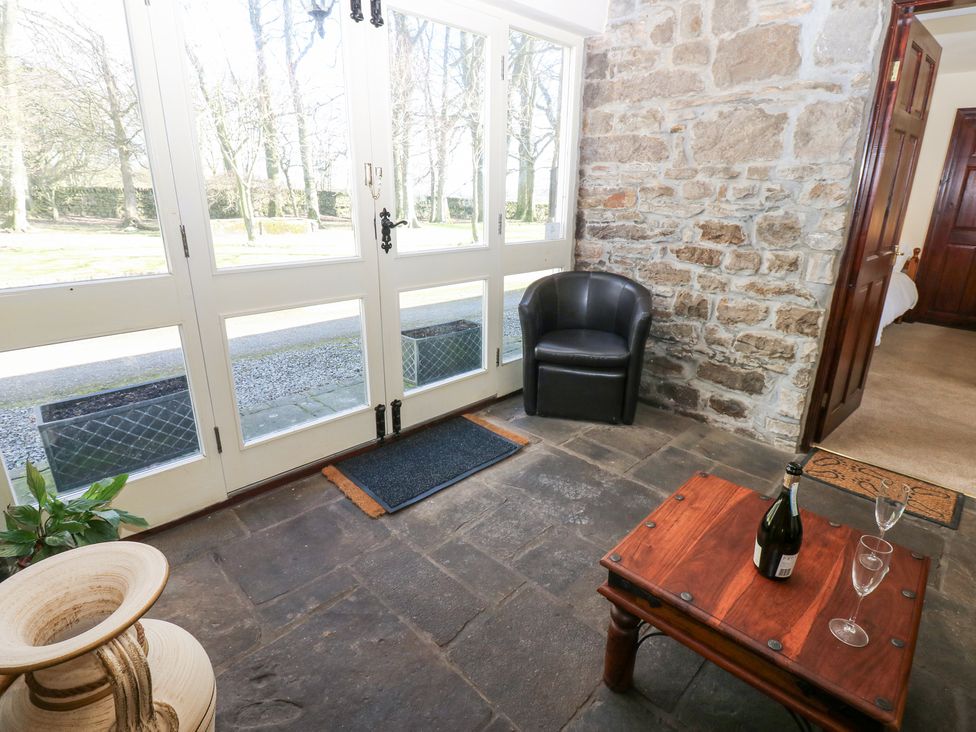 A sitting area with a wooden table holding a bottle and two glasses a black chair and a stone wall at Pencroft Cottage in Carperby