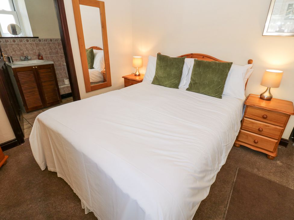 A bedroom with a double bed two green pillows two wooden nightstands with lamps a full-length mirror and a bathroom sink at Pencroft Cottage in Carperby