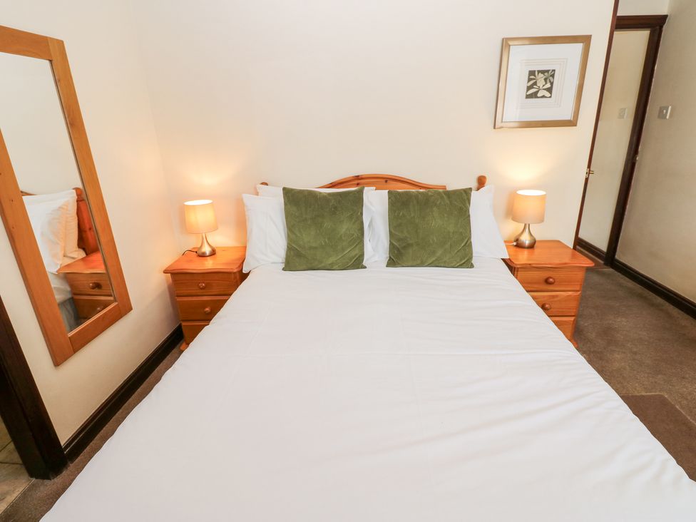 A bedroom with a double bed two green pillows two bedside tables with lamps a large mirror and a framed picture at Pencroft Cottage in Carperby