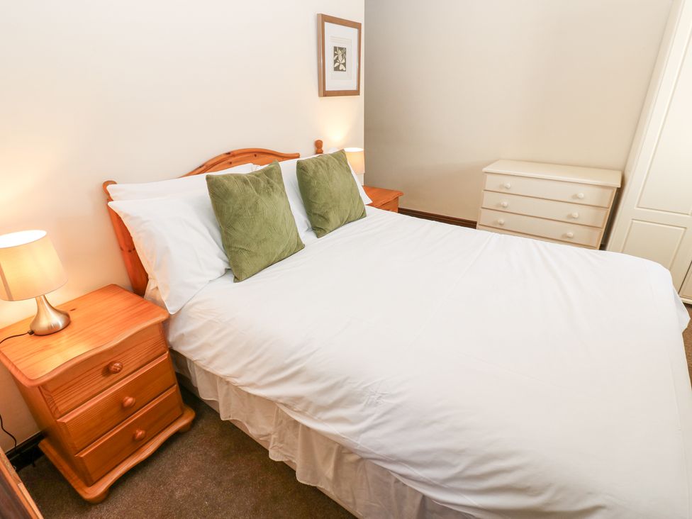 A bedroom with a double bed two green pillows wooden bedside tables with lamps a chest of drawers and a wardrobe at Pencroft Cottage in Carperby