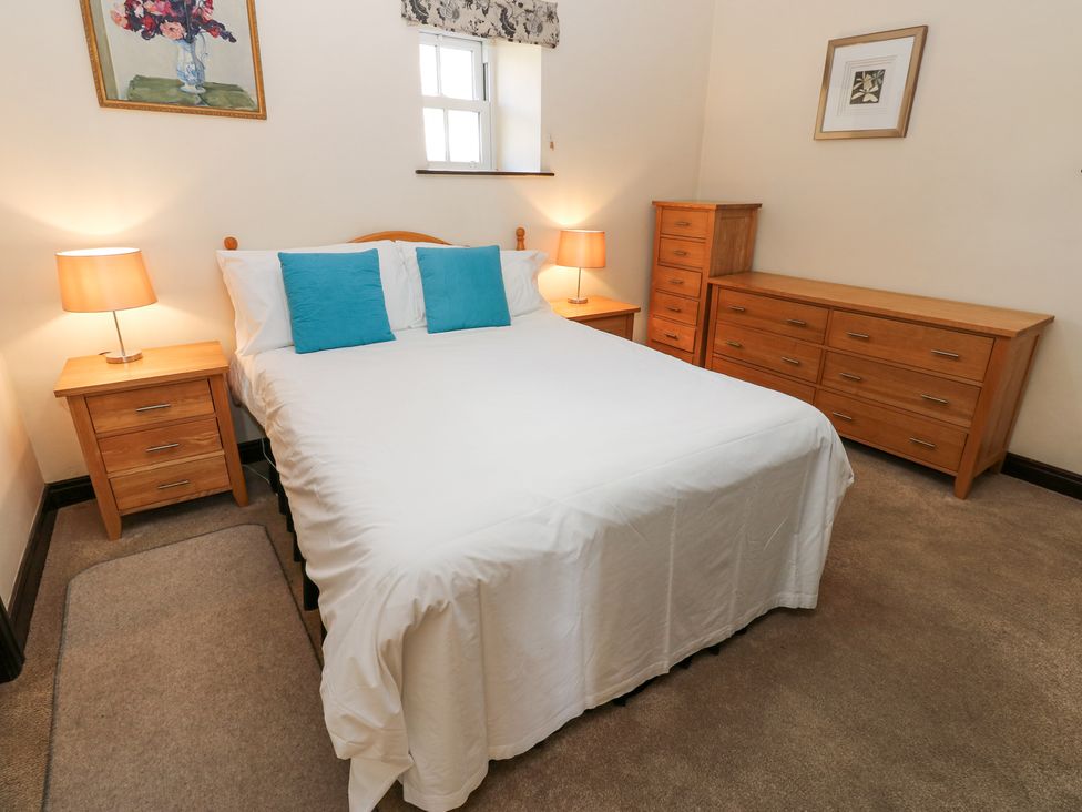 A bedroom with a bed with blue pillows two bedside tables with lamps and wooden dressers at Pencroft Cottage in Carperby