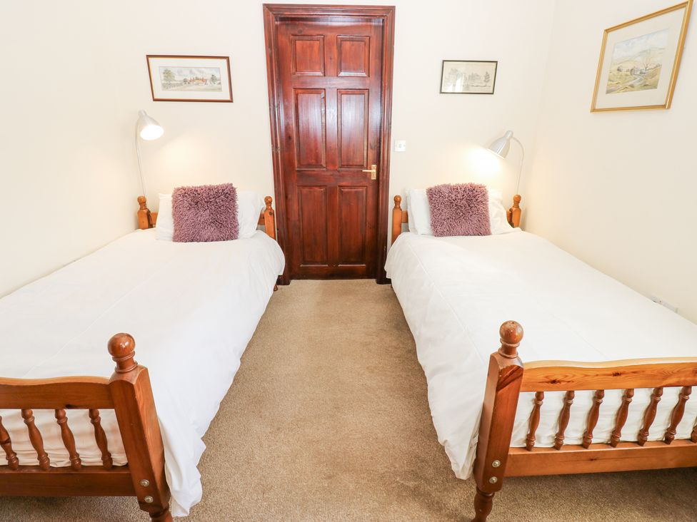A bedroom with two single wooden beds with white bedding and purple cushions and a wooden door between them at Pencroft Cottage in Carperby