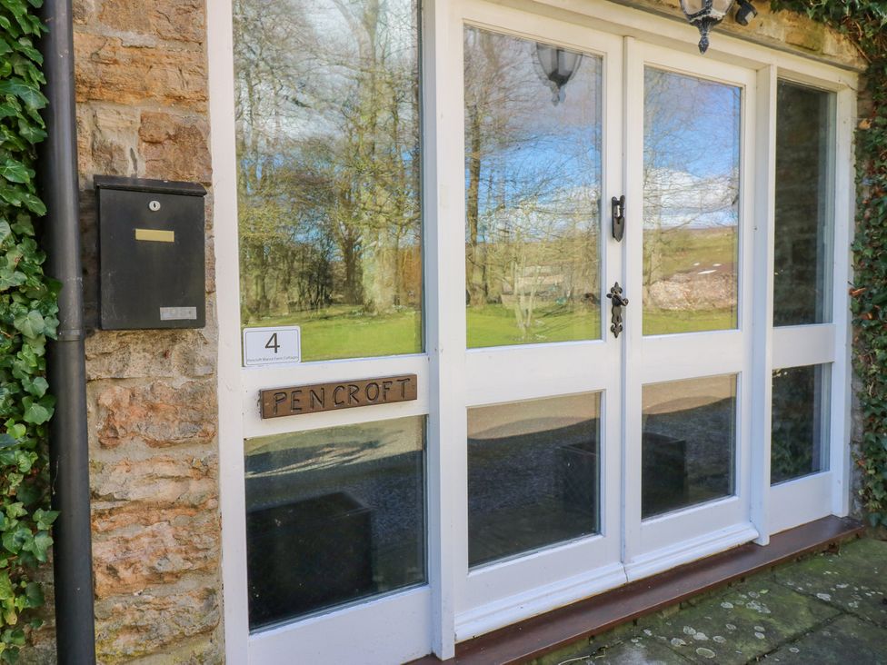 A white wooden door with glass panels and a black mailbox on a stone wall at Pencroft Cottage in Carperby