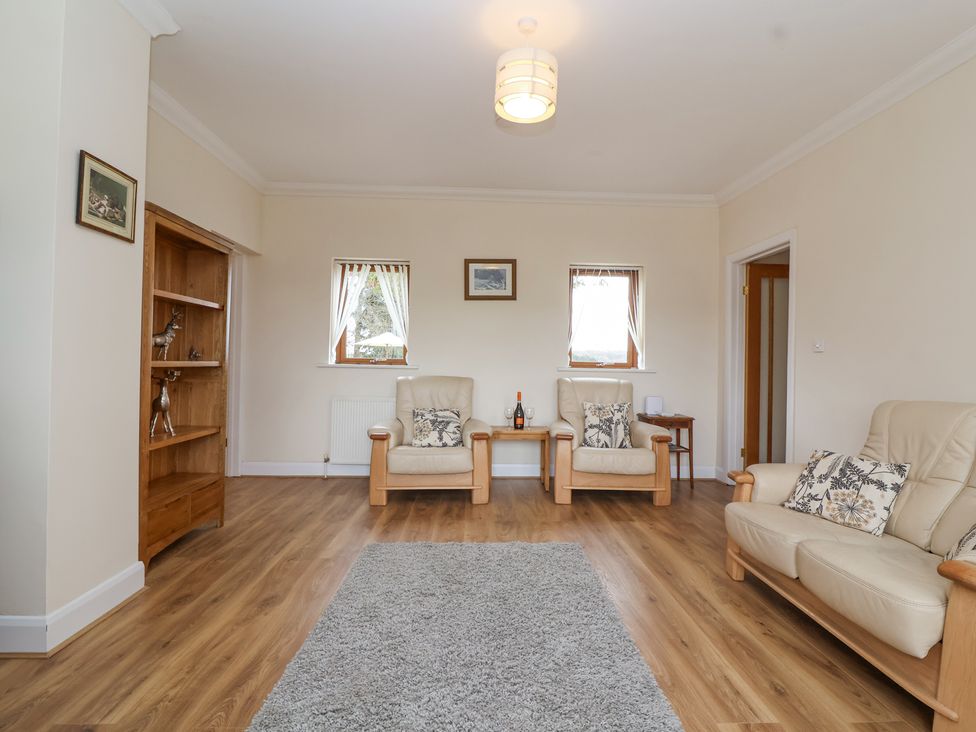 A living room with two armchairs, a sofa, a wooden shelving unit, two small tables, and a rug on wooden flooring at Stapleton Farm Bungalow Damerham near Alderholt