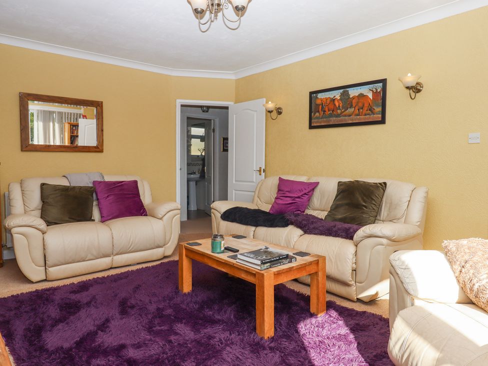 A living room with two beige sofas with cushions a wooden coffee table with books and a candle a large purple rug a mirror on one wall and a painting of elephants on another wall at House of Emma in Paignton