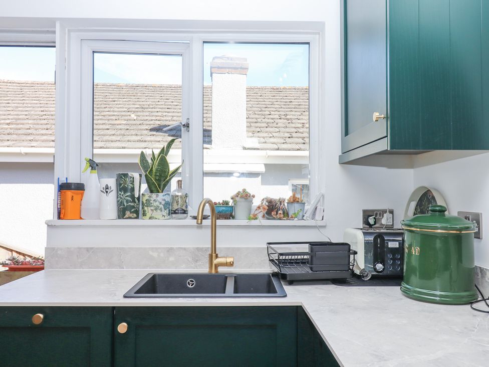 A kitchen sink with gold faucet green cabinets and items on the countertop and windowsill at House of Emma in Paignton
