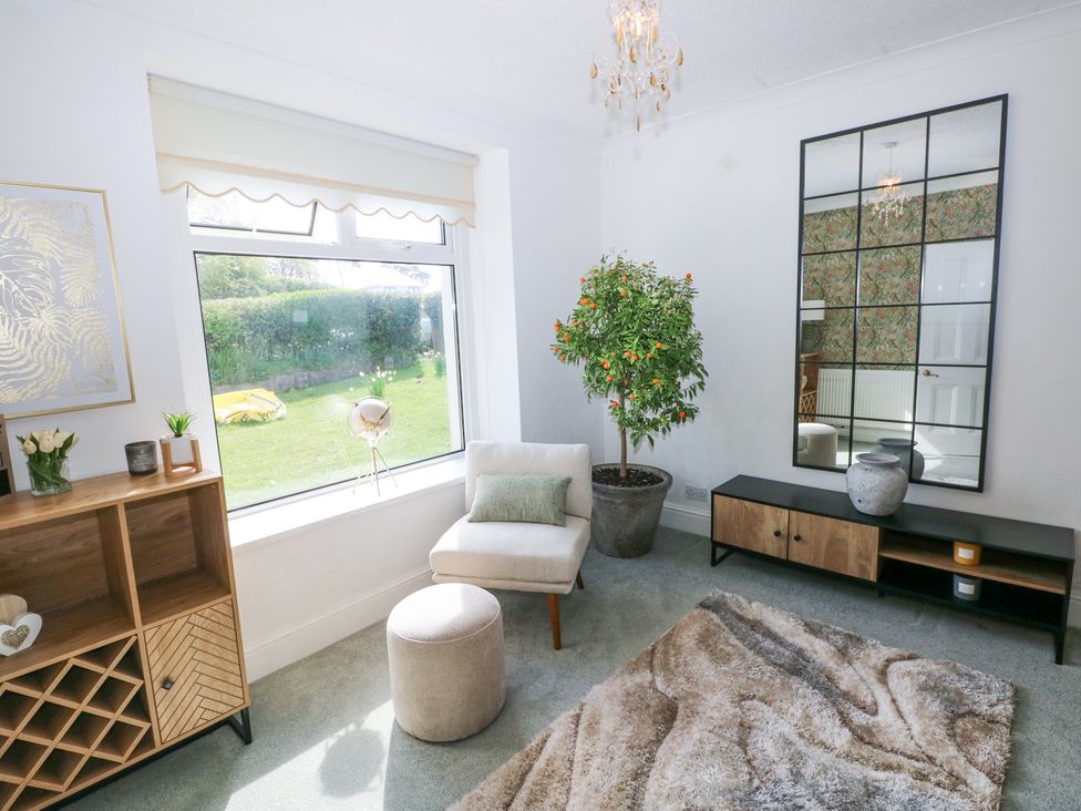 A sitting room with a window seat, small armchair with ottoman, potted plant, console table, wall mirror, and wooden storage unit at Burry House in Llanmorlais