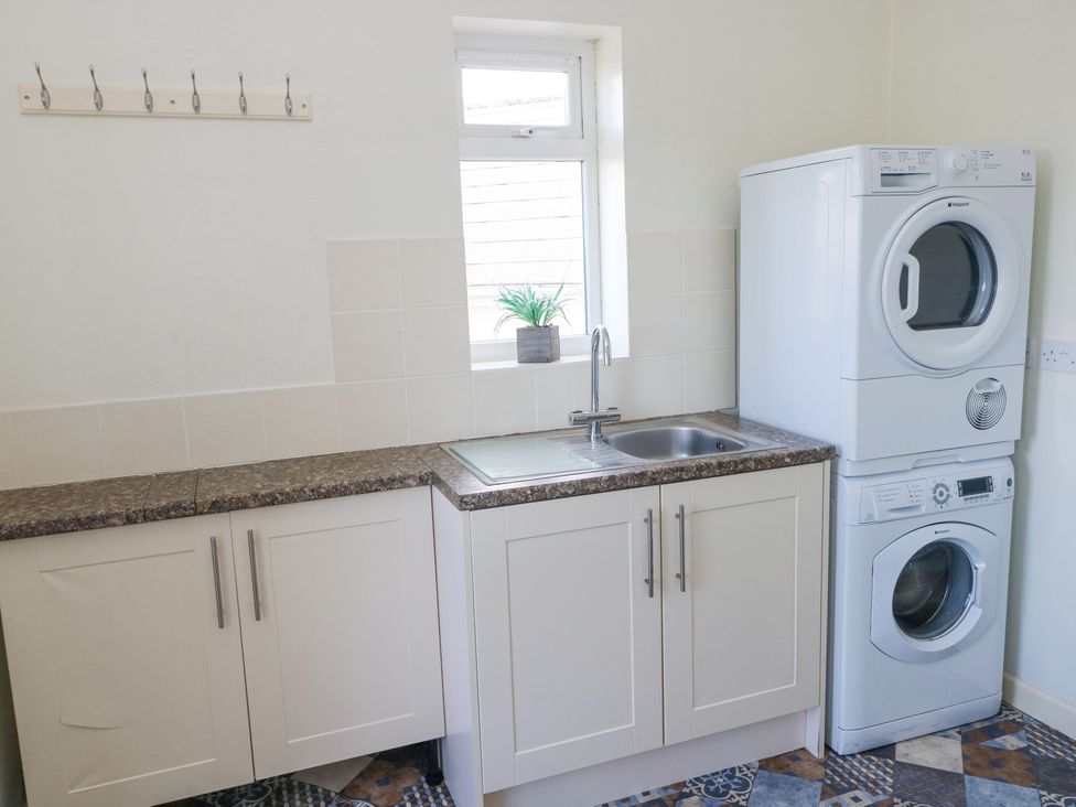 A laundry room with a stackable washer and dryer next to a sink and counter with white cabinets at Burry House in Llanmorlais