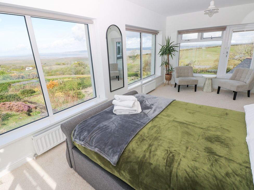 A bedroom with a bed near corner windows and two chairs around a small table at Burry House in Llanmorlais