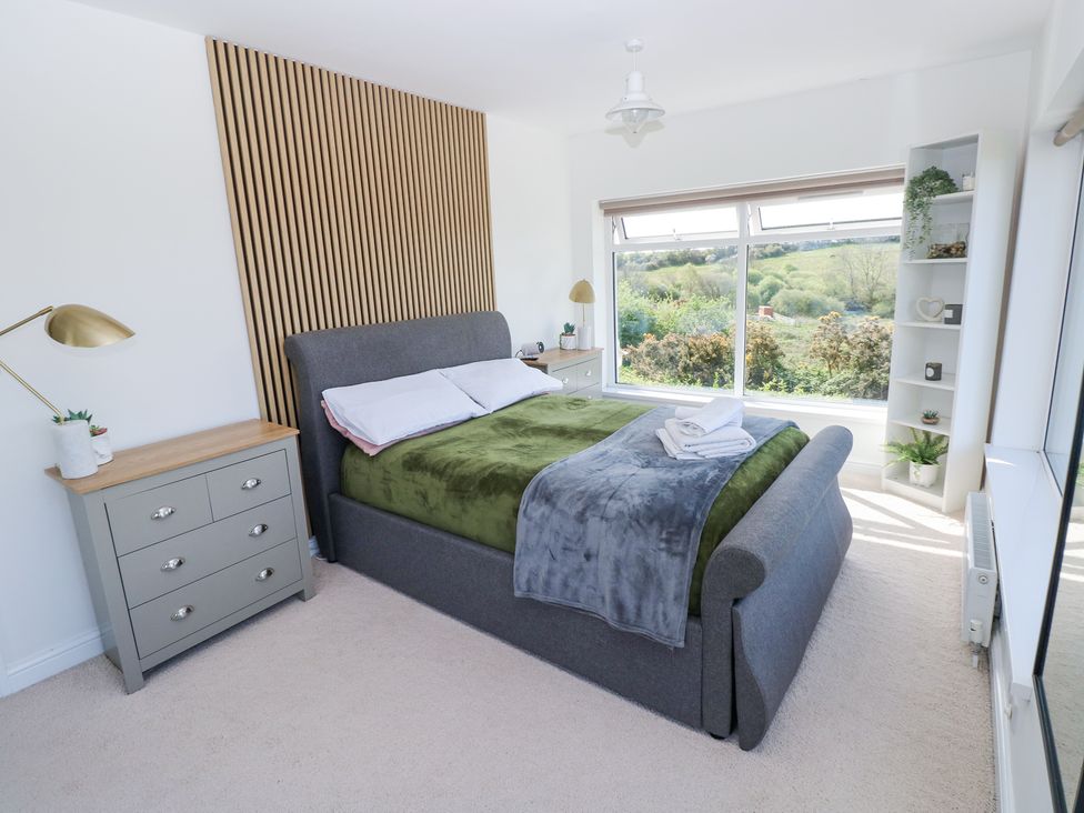 A bedroom with a gray bed and green blanket next to a window with a scenic view at Burry House in Llanmorlais