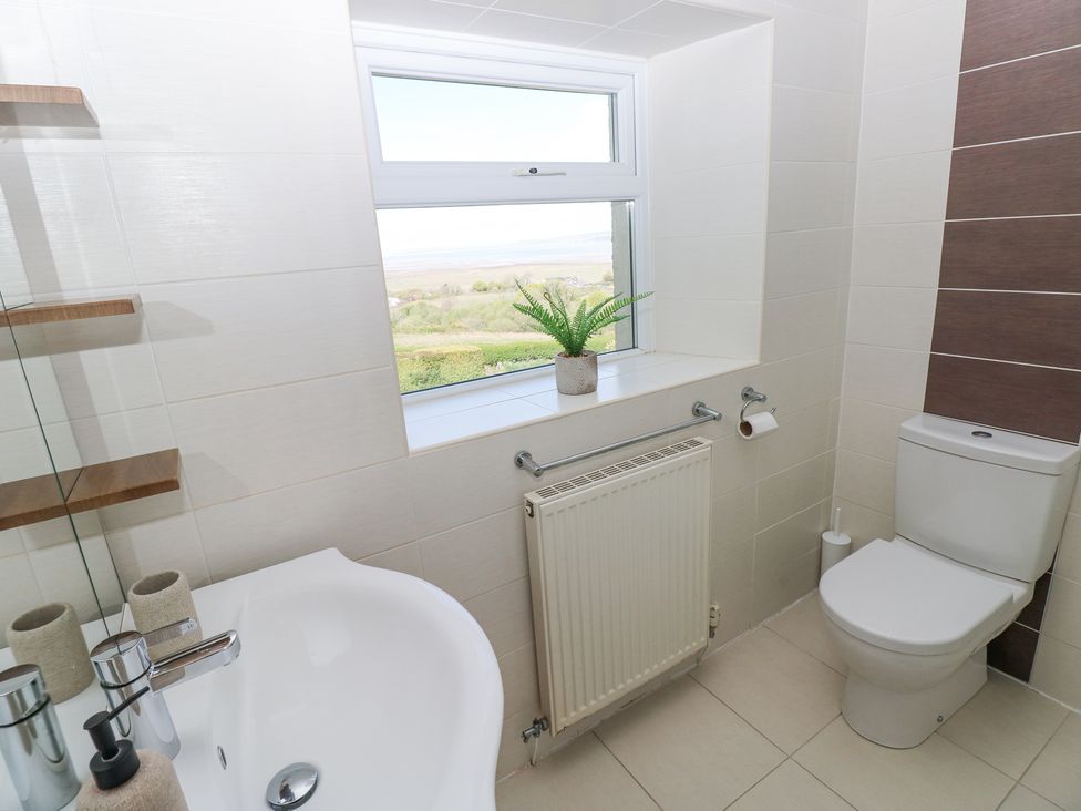 A bathroom with a white sink and faucet a toilet a window with a small plant on the sill and a radiator below the window at Burry House in Llanmorlais