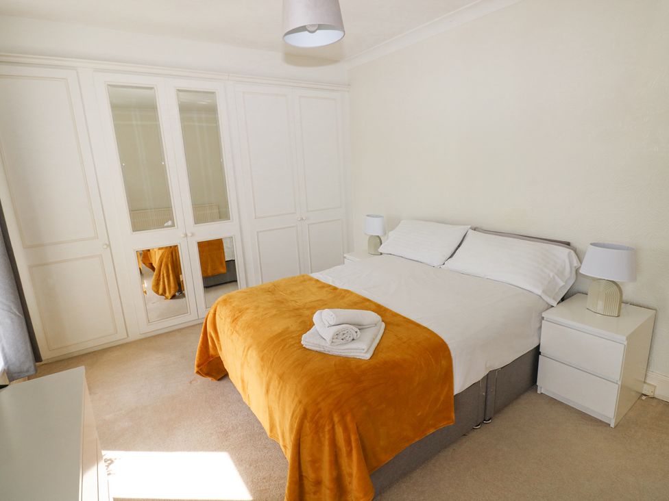 A bedroom with a bed covered with white bedding and a mustard colored blanket two bedside tables with lamps and a large wardrobe with mirrored panels at Burry House in Llanmorlais