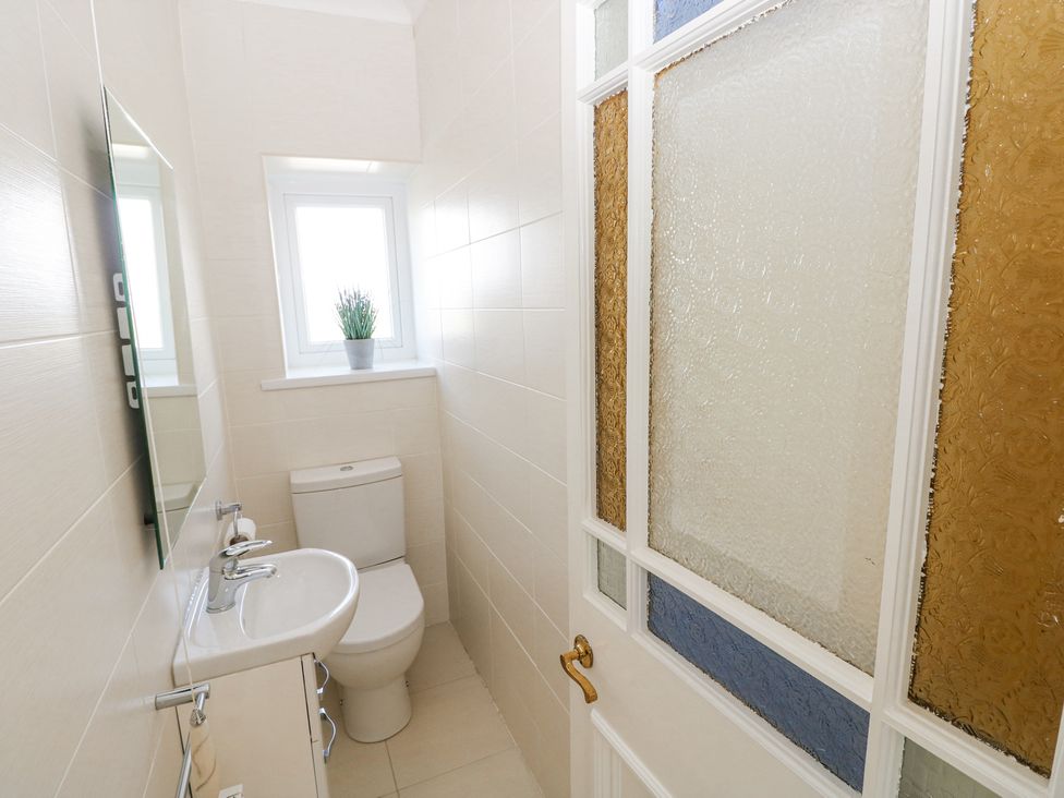 A small bathroom with a toilet sink mirror window and a door with colored glass at Burry House in Llanmorlais