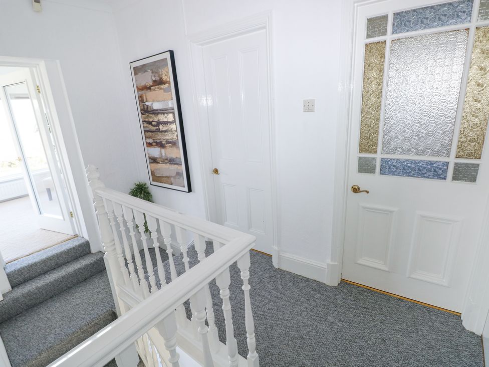 A hallway with blue carpet stairs white doors and a framed painting at Burry House in Llanmorlais