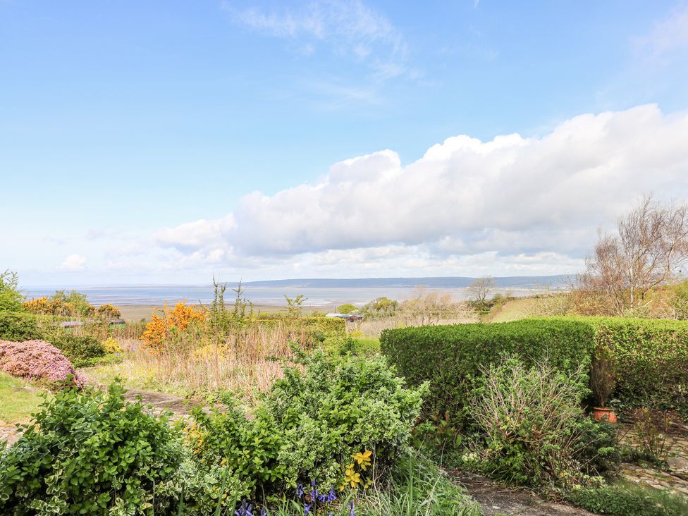 A garden with various bushes and flowering plants overlooking a body of water under a partly cloudy sky at Burry House in Llanmorlais