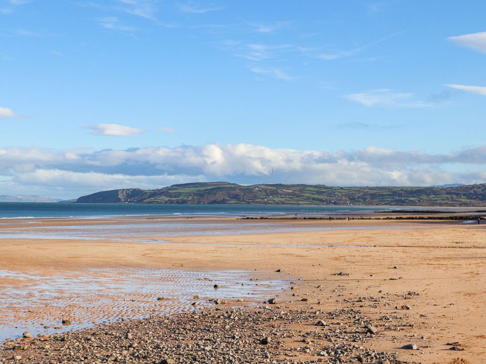 A sandy beach with scattered rocks and a distant green hillside near Cae Coch in Brynteg near Benllech