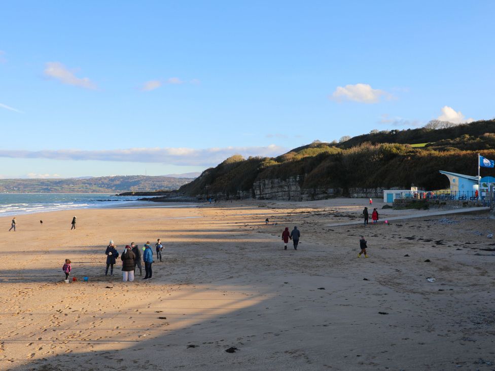 A sandy beach with people walking and playing near cliffs and buildings at Cae Coch in Brynteg near Benllech