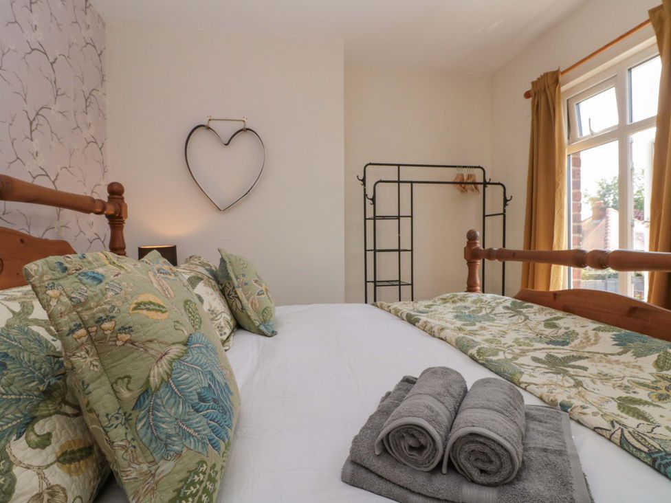 A bedroom with a bed, towels, and a clothing rack at Moot Cottage in Driffield