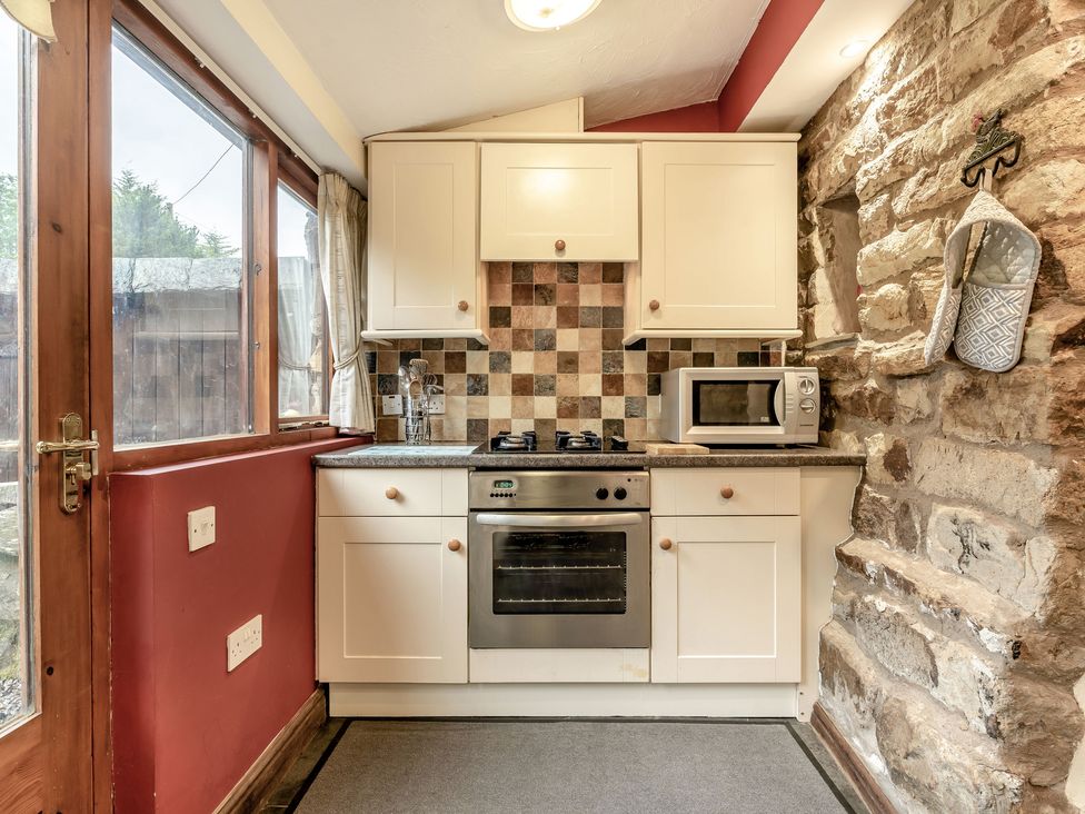 A kitchen with cream cabinets a gas stove an oven a microwave a checkered tile backsplash and a stone wall at Brant View in Cautley near Sedbergh