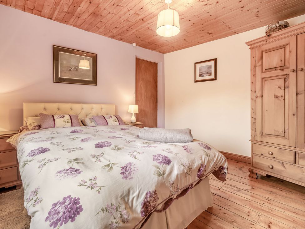 A bedroom with a bed with floral bedding wooden furniture and framed pictures at Brant View in Cautley near Sedbergh